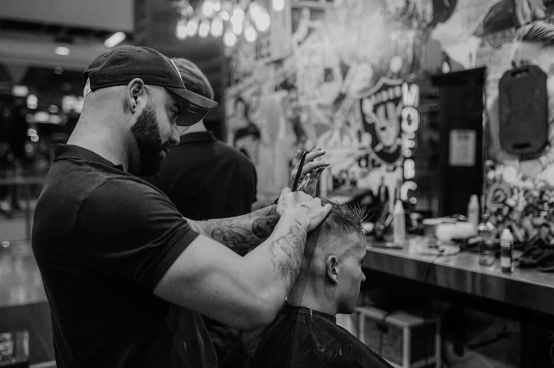 Барбер крепкого телосложения в чёрной бейсболке подстригает клиента