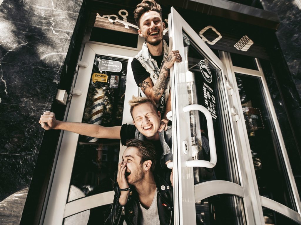 Компания друзей весело улыбается стоя возле входа в помещение