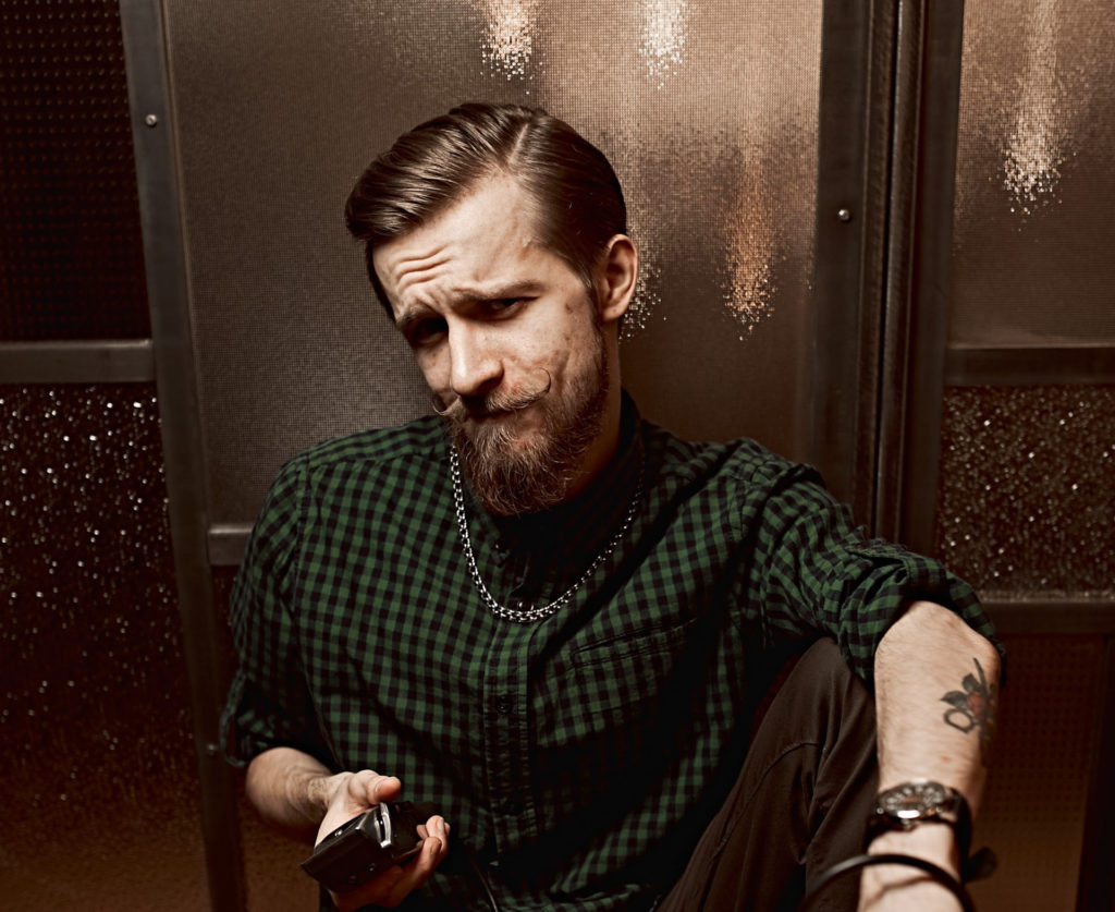 Мужчина средних лет позирует на камеру сморщив лоб держа в руке машинку для стрижки