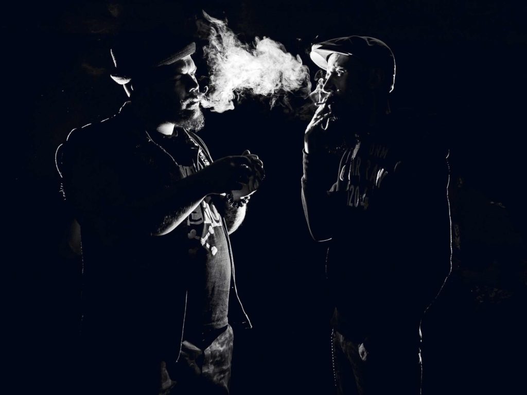 Два мужчины смотрят друг на друга в полумраке и курят